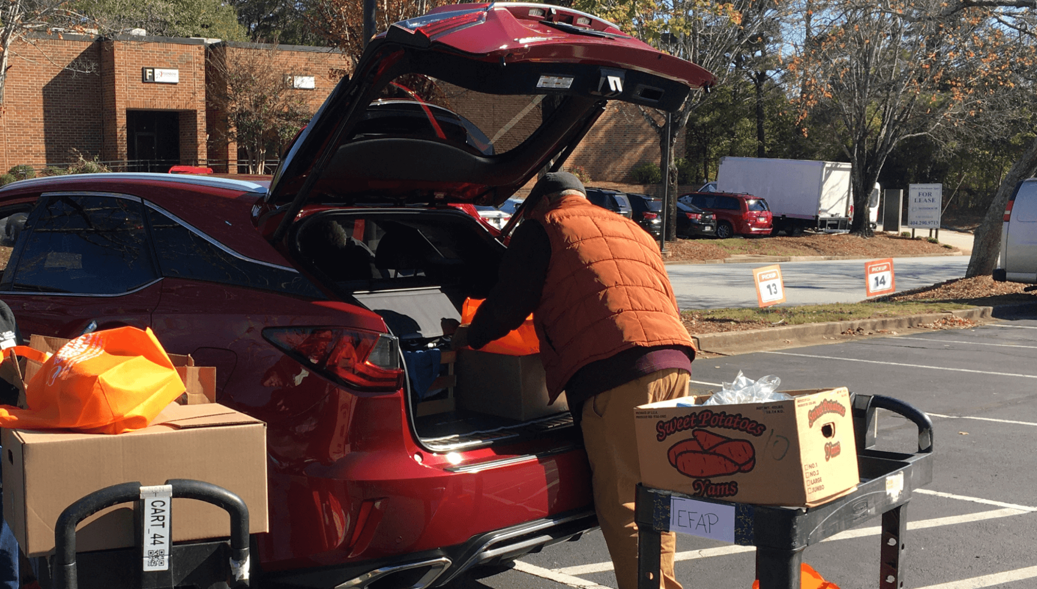 Man loading boxes of yams in/out of trunk of car.